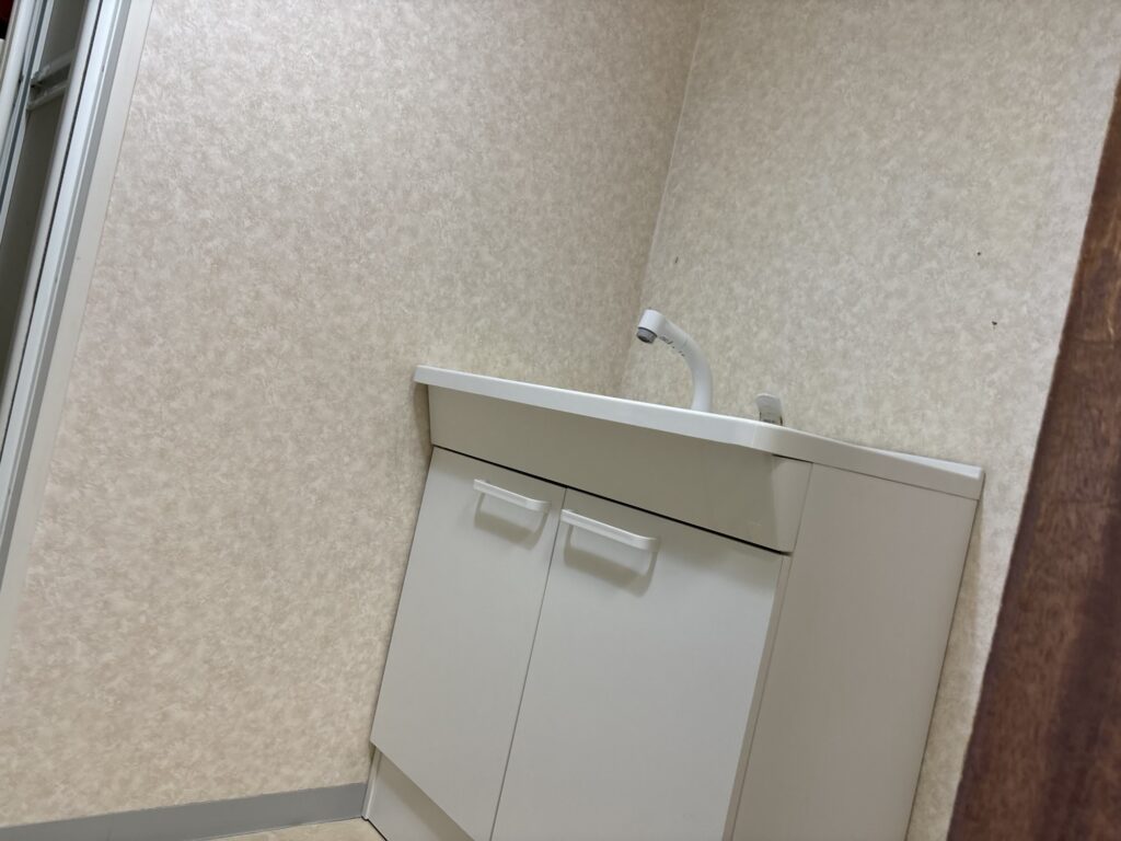 Laundry room vanity before renovation with existing wallpaper and fixtures in an occupied home.