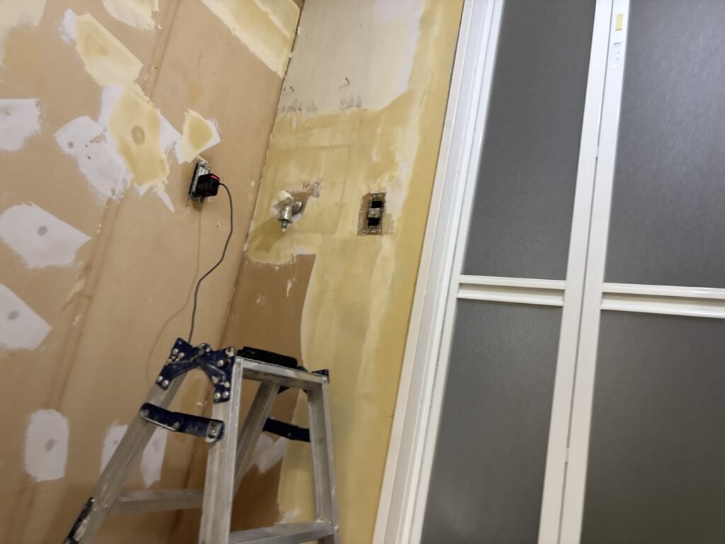 Laundry room wall fully prepared with finishing compound before patterned wallpaper installation.