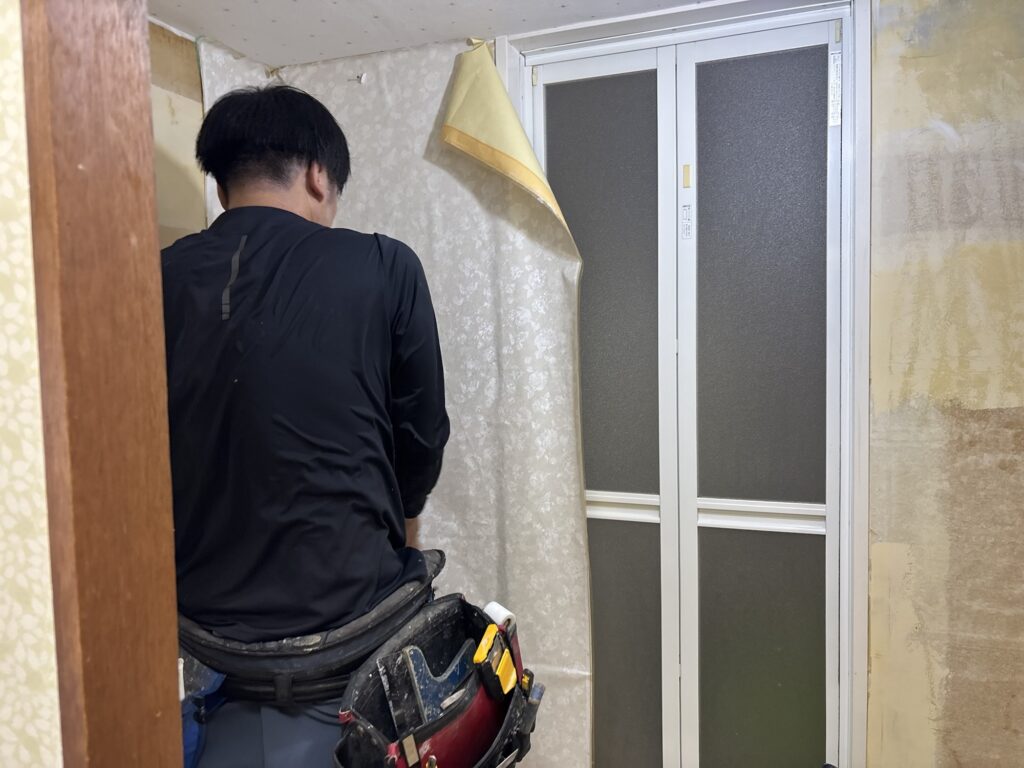Wallpaper installer matching the patterned wallpaper on a laundry room wall.