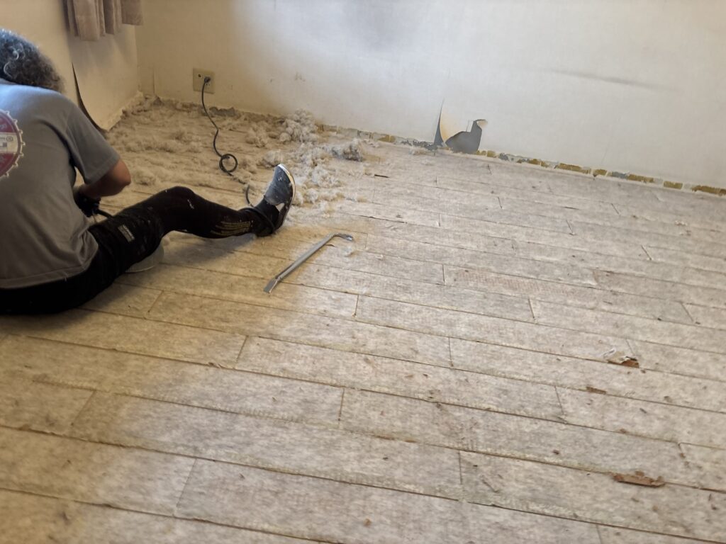 Worker using a power sander to remove white cushion backing from a subfloor