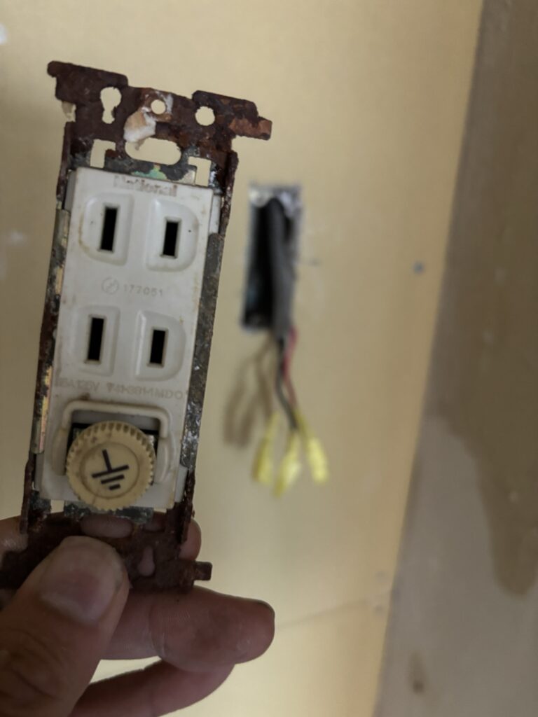 Close-up photo of a removed electrical outlet showing clear signs of rust and corrosion on the metal parts.