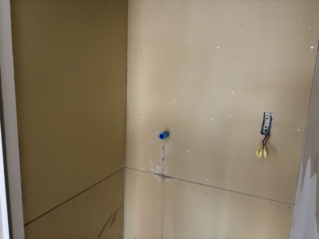 Laundry room wall with electrical outlet and plumbing fixtures removed before drywall installation.