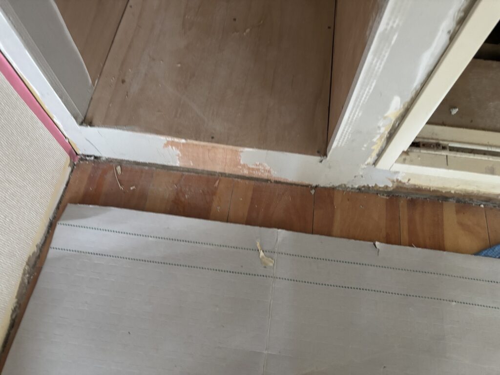 Close-up photo showing a noticeable gap between the existing floor tiles and the wooden floor of the shelf unit.