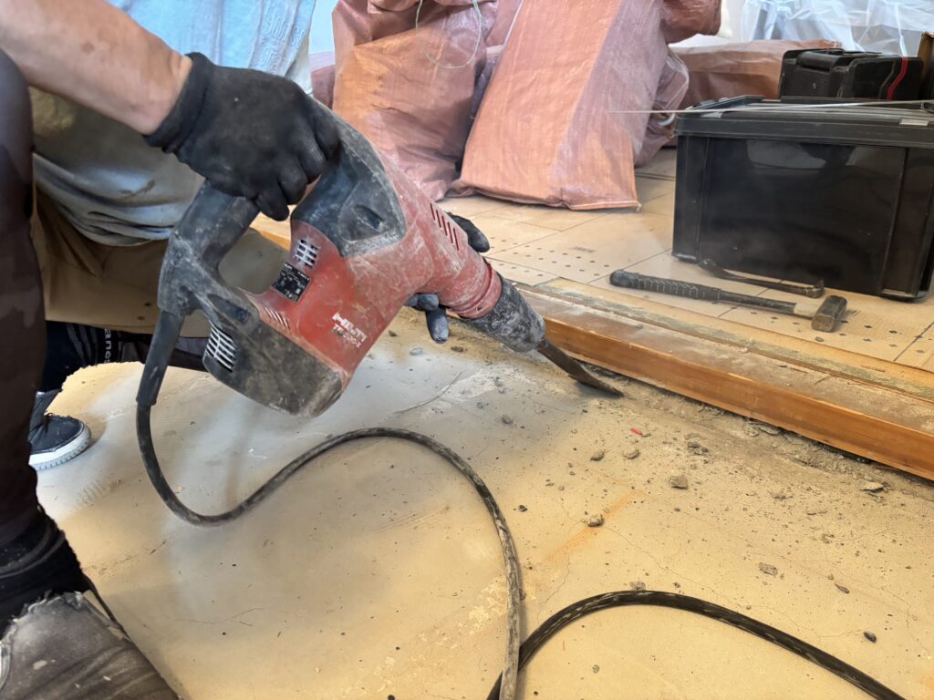 Worker removing leftover mortar from the edge of a concrete subfloor
