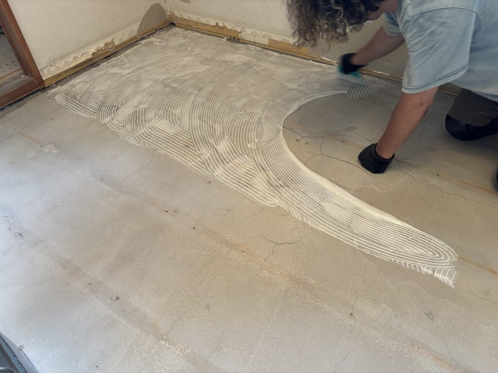 Construction adhesive being applied to the floor before plywood subfloor installation