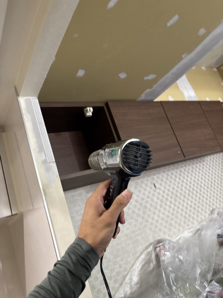 Wallpaper installer using a heat gun to dry joint compound before wallpaper installation.