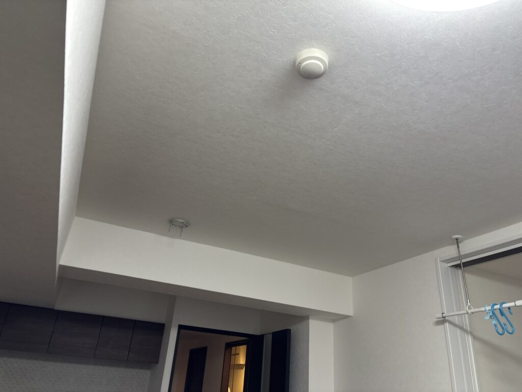 Finished ceiling and beam with newly installed wallpaper in a Japanese condominium living room.