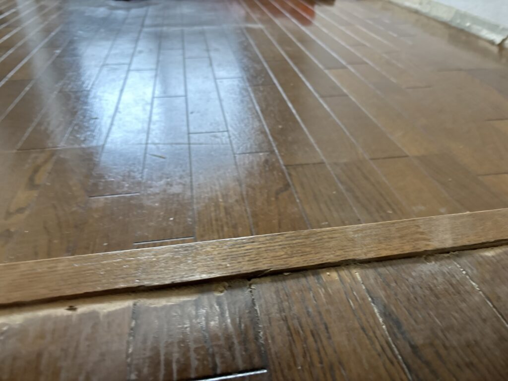 Existing floor transition trimmed with a utility knife to reduce its height before vinyl flooring installation.