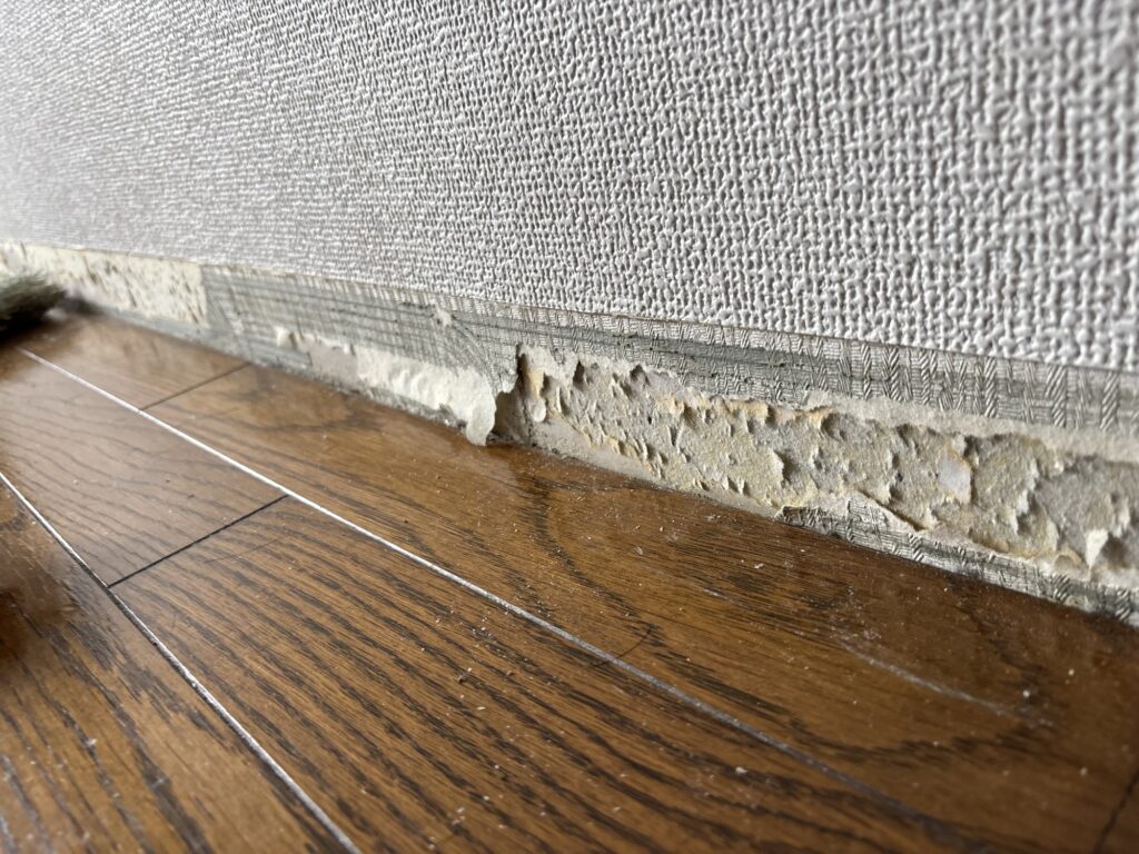 Old soft vinyl baseboard removed from the wall before new vinyl flooring and baseboard installation.