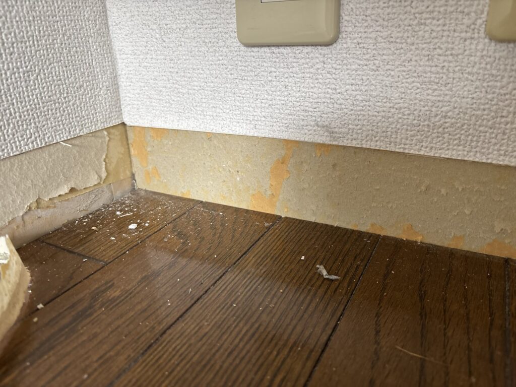 Old loose wallpaper being removed from underneath a soft baseboard before installing new baseboard.