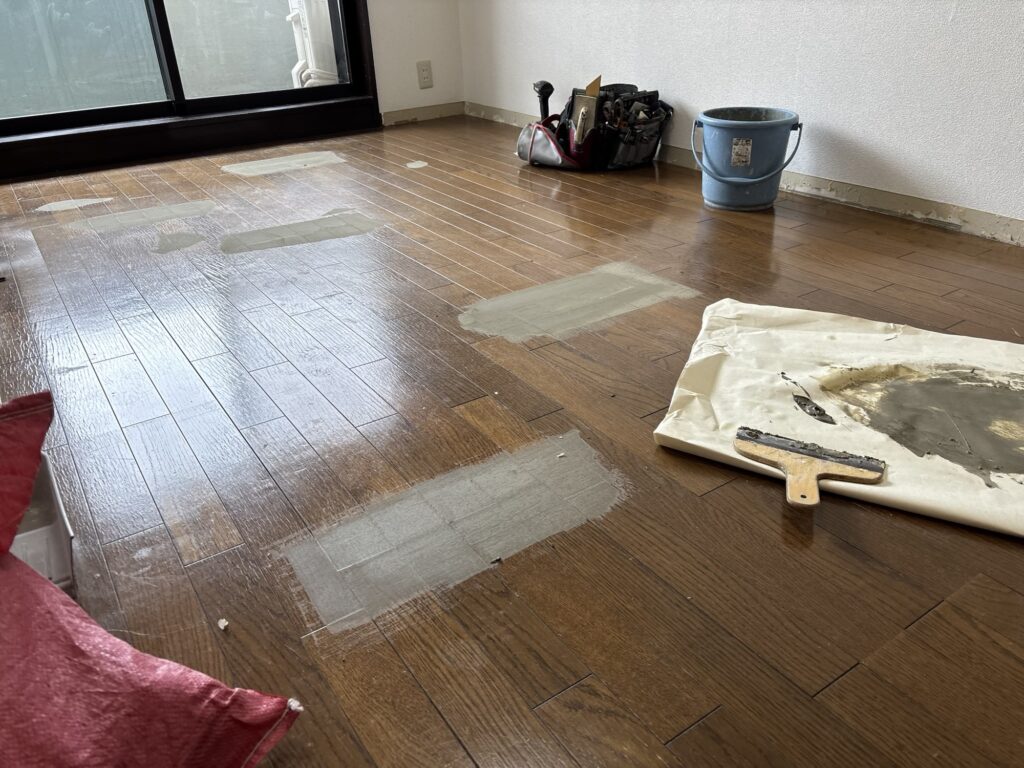Floor filler being applied to a damaged section of wood flooring before vinyl flooring installation.