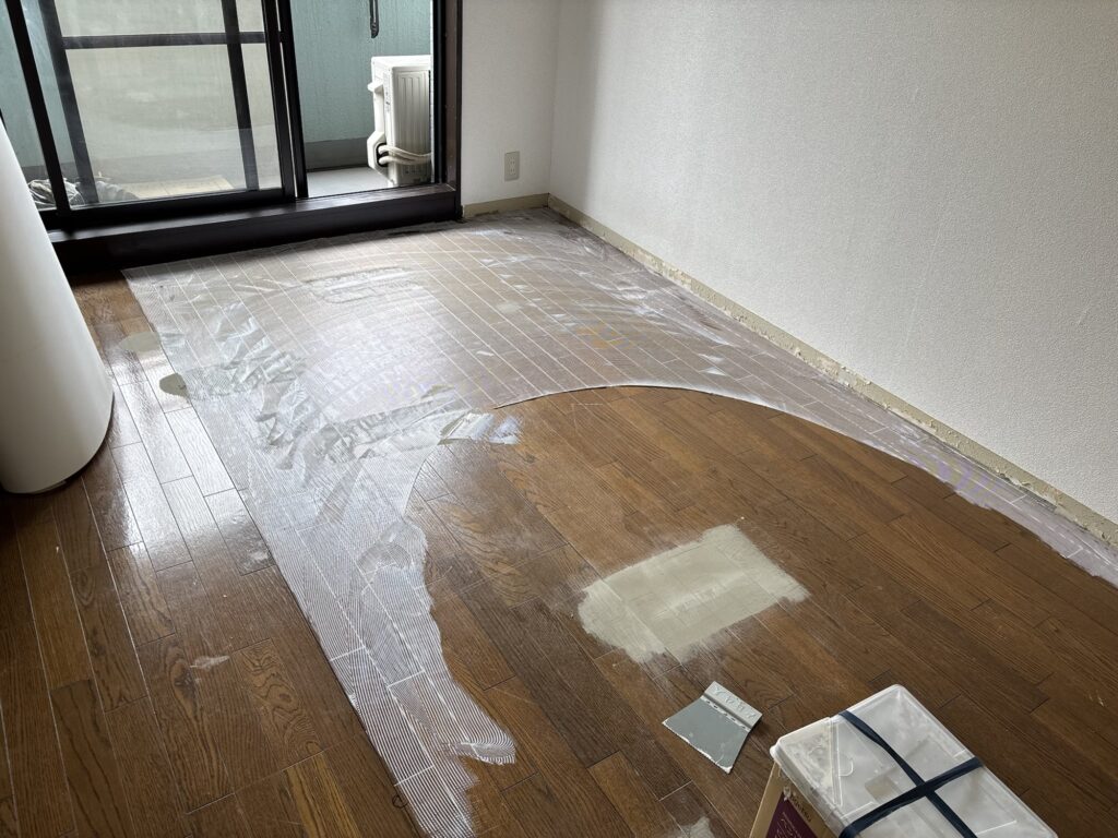 Flooring adhesive being spread evenly across the wood floor before vinyl flooring installation.