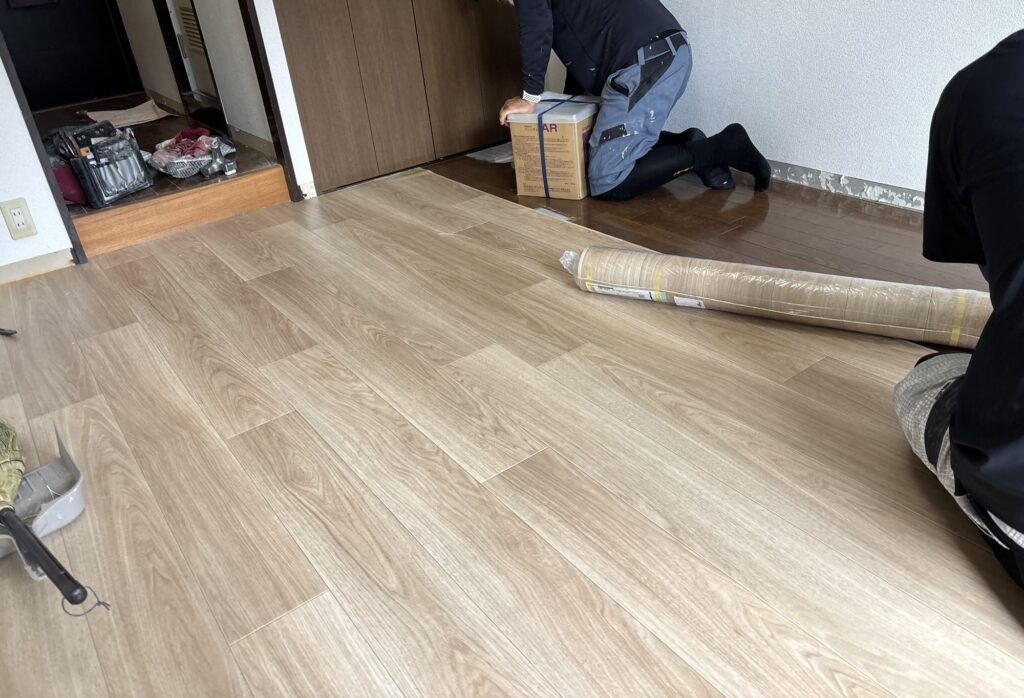 Worker applying adhesive to the floor before installing the second sheet of vinyl flooring.