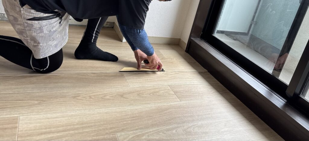Worker cutting a vinyl flooring joint through two overlapping sheets using a large-blade utility knife.