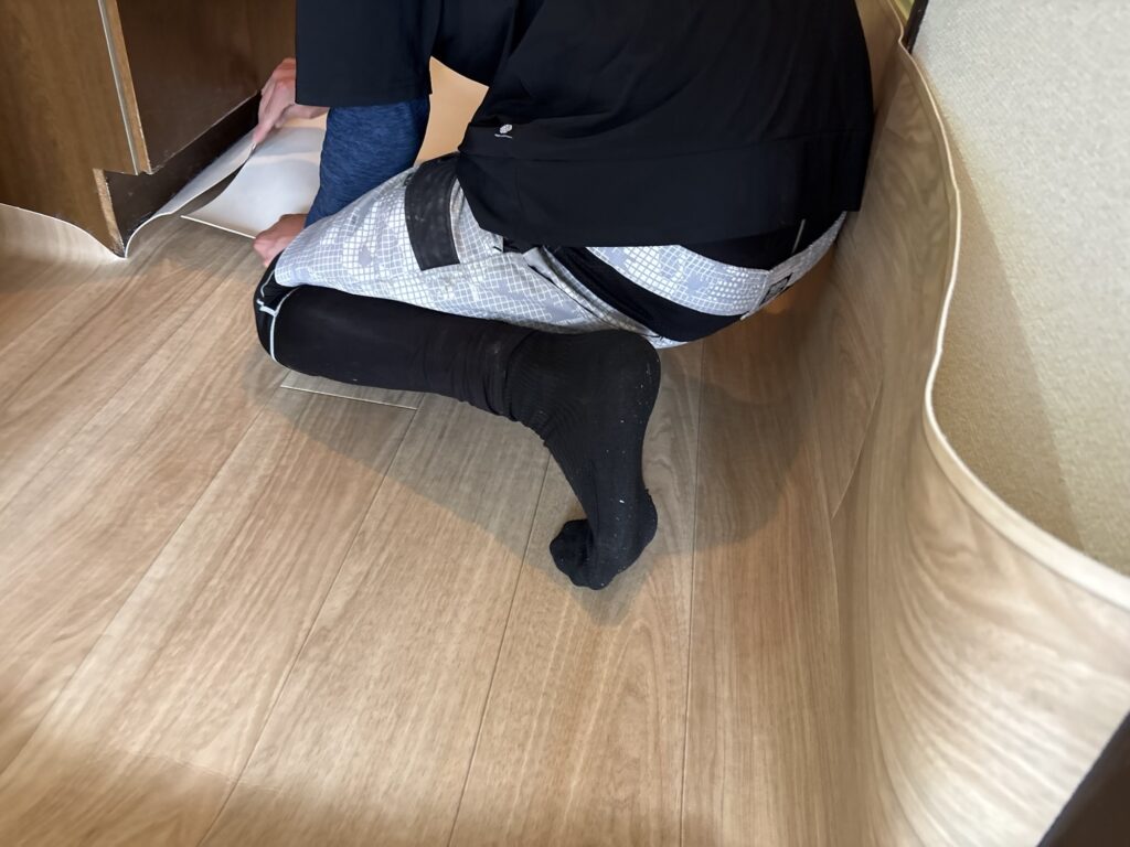 Worker installing cushion vinyl flooring in the kitchen of a Japanese apartment.