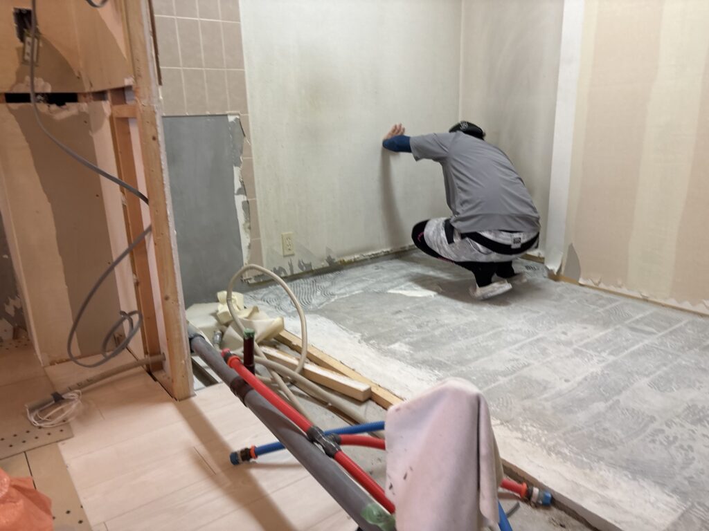 Worker applying adhesive to the subfloor before installing new wood flooring.