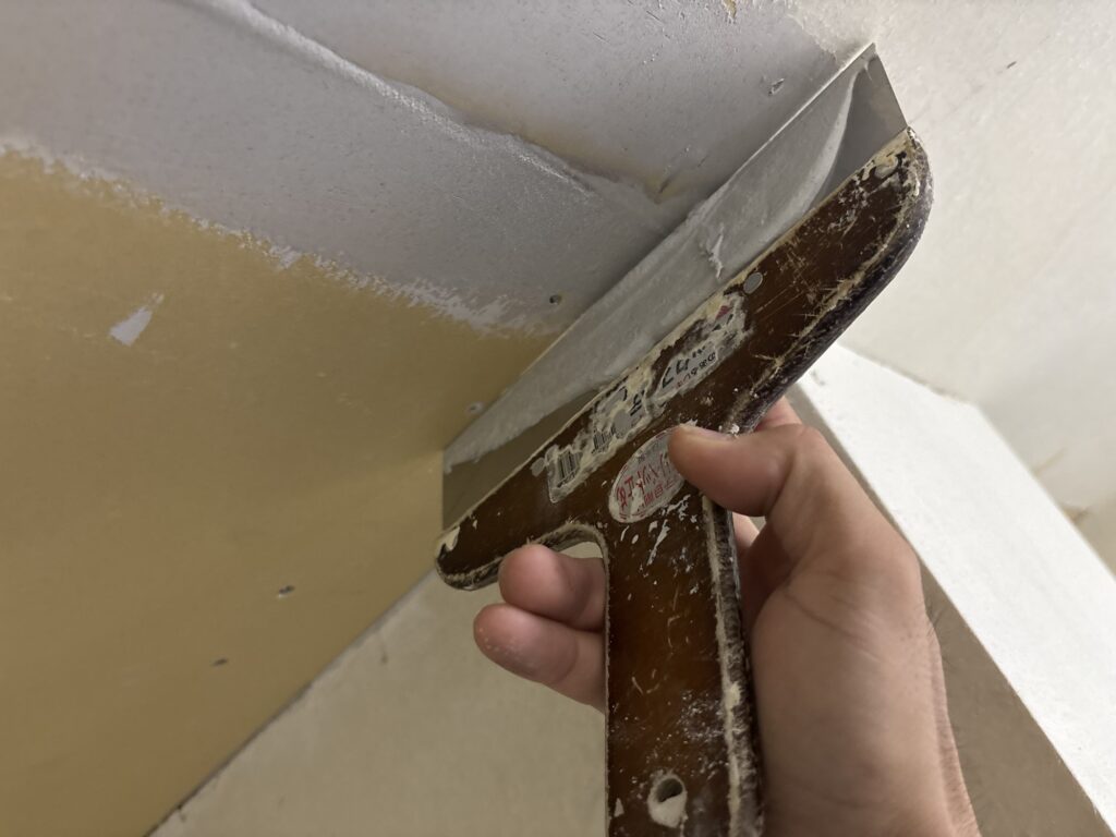 Wallpaper installer using a putty knife to apply joint compound to a repaired ceiling.