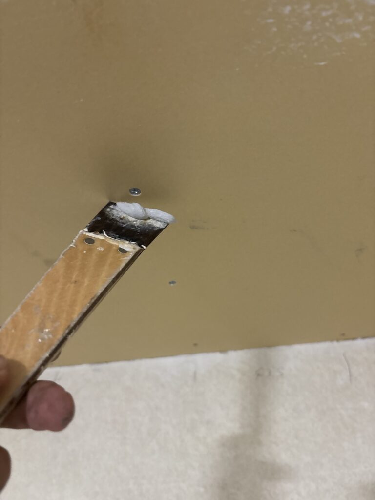 Worker using a small putty knife to fill screw holes in newly installed gypsum board.