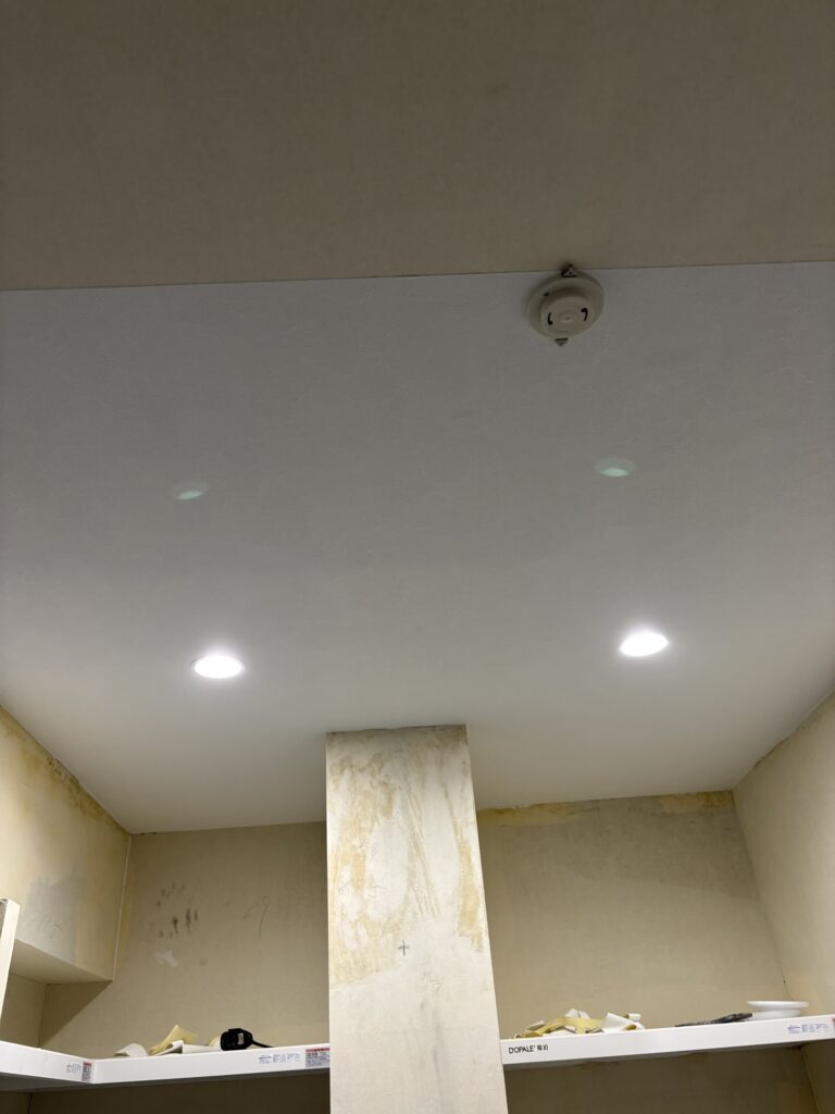 Two wallpaper installers applying white stone-pattern wallpaper to an apartment ceiling.