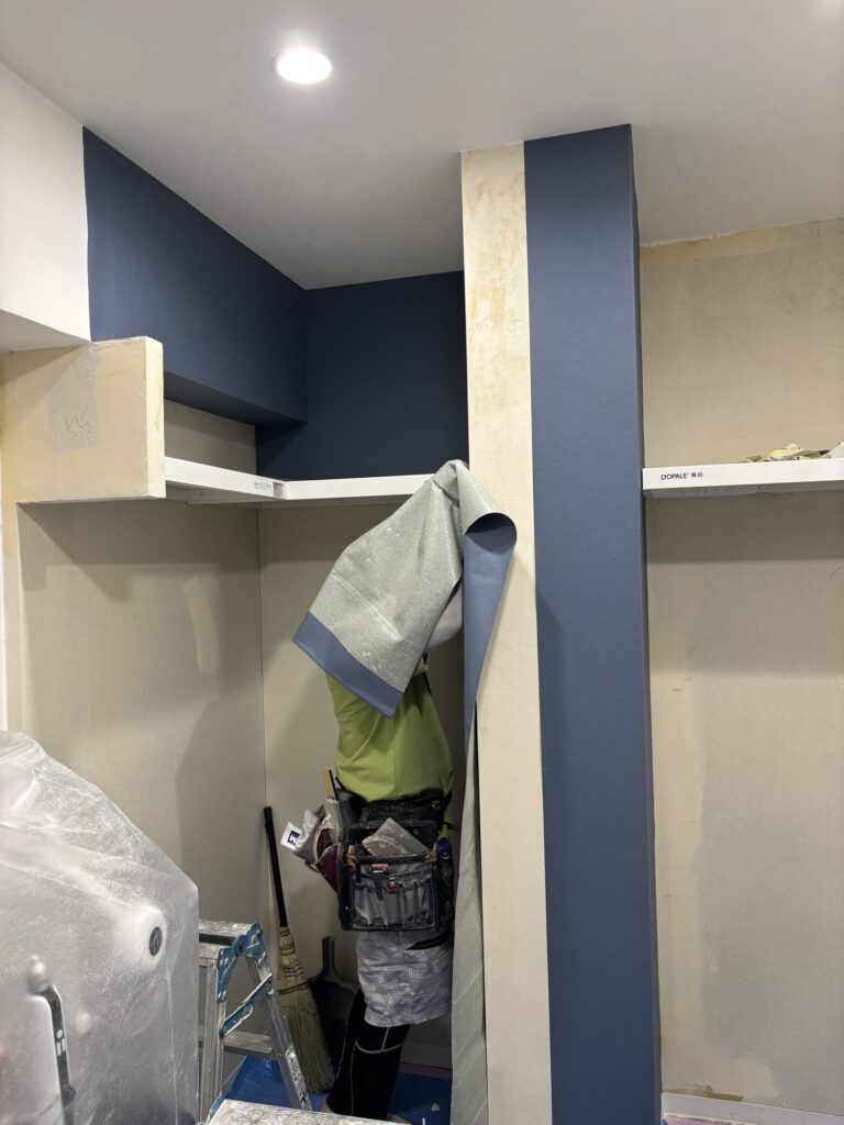 Wallpaper installer applying navy blue wallpaper to the walls of a Japanese apartment.