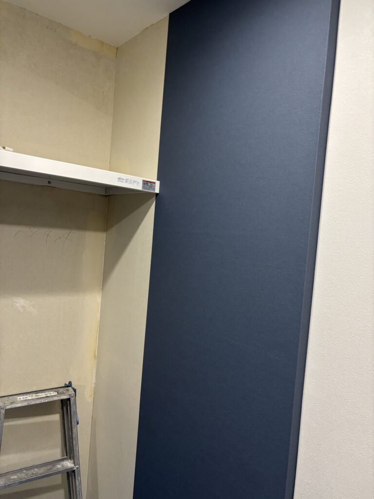 Worker installing navy blue wallpaper on an apartment wall during renovation.