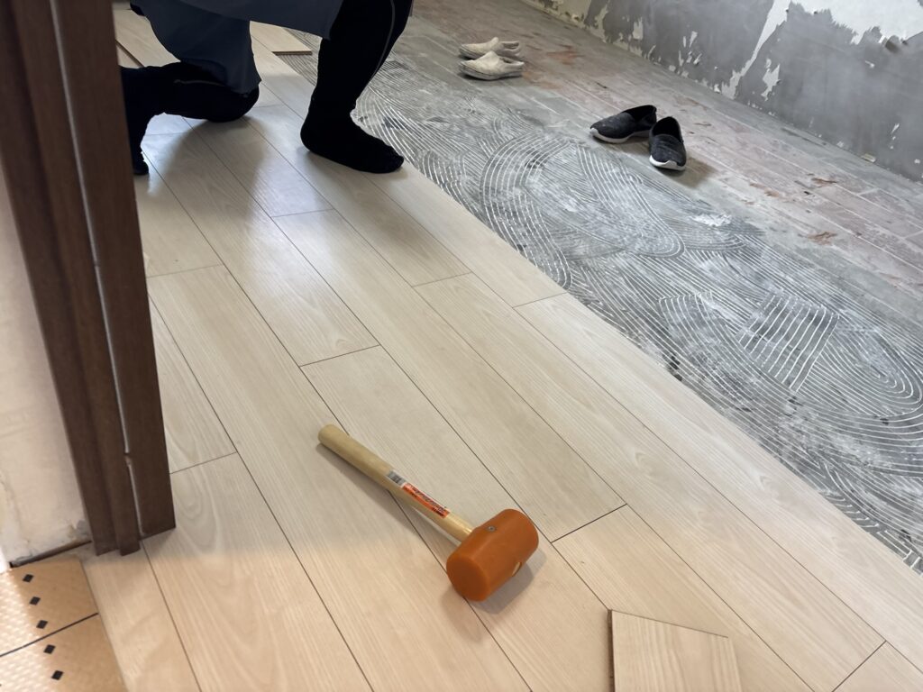 Worker using a rubber mallet to close a small gap between flooring boards.