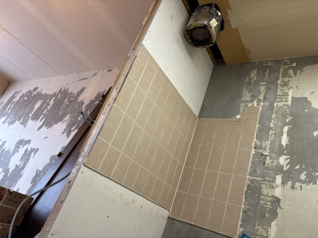 Worker removing old kitchen tiles with a pry bar and hammer during apartment renovation.
