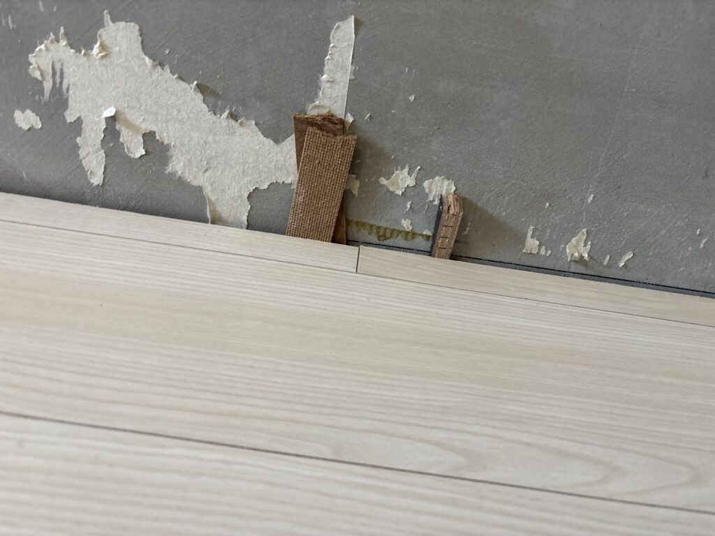 Wedges securing newly installed flooring along the edge while the adhesive cures.