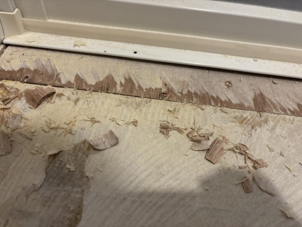 Worker trimming excess plywood near the bathroom entrance with a utility knife.