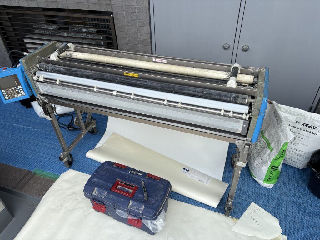 Wallpaper being coated with adhesive using a wallpaper pasting machine.