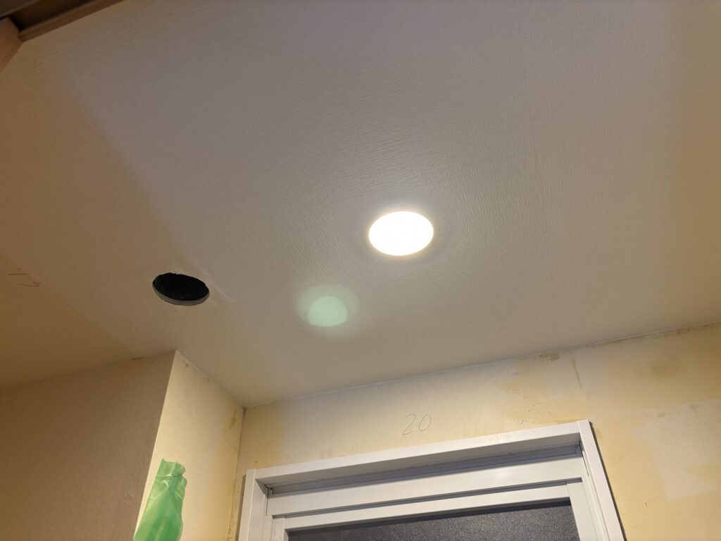 Worker installing embossed wallpaper on a bathroom ceiling.