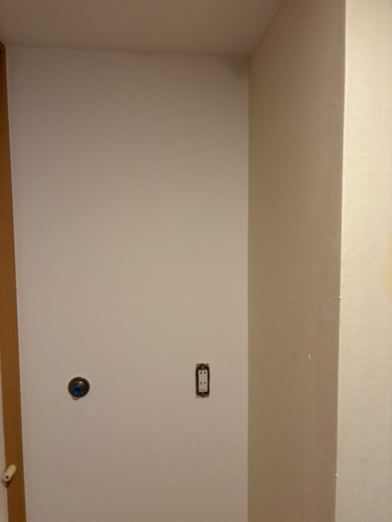 Wallpaper being cut around a washing machine water supply connection.