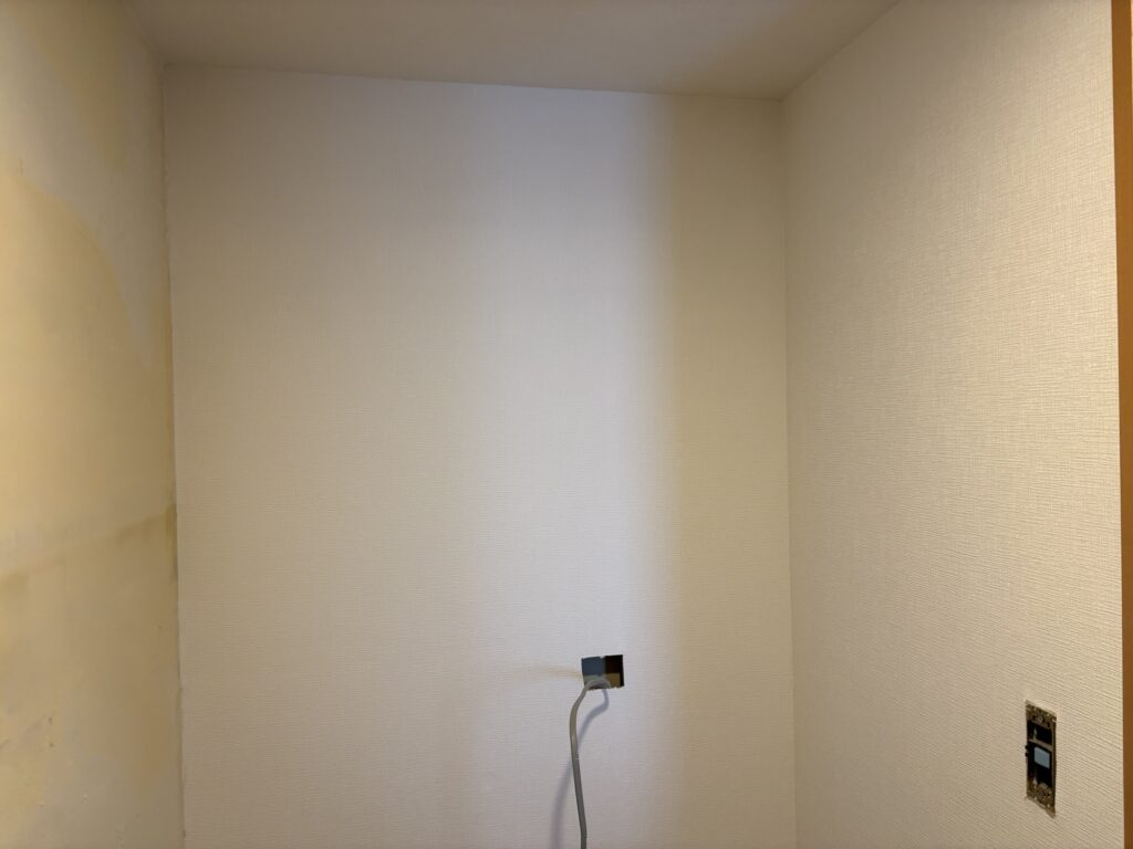 Worker installing embossed wallpaper on the walls of a bathroom vanity and laundry area.