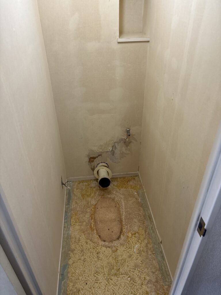 Toilet floor and walls after the old wallpaper and vinyl flooring have been removed