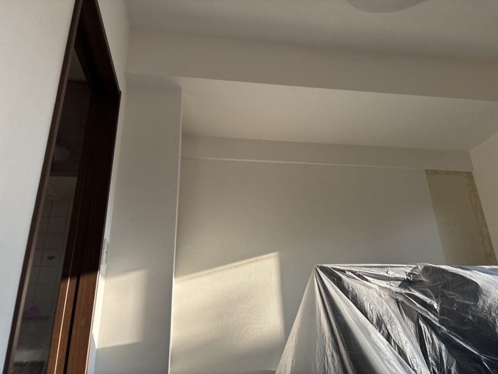 Wallpaper installer applying white wallpaper to another section of a living room wall