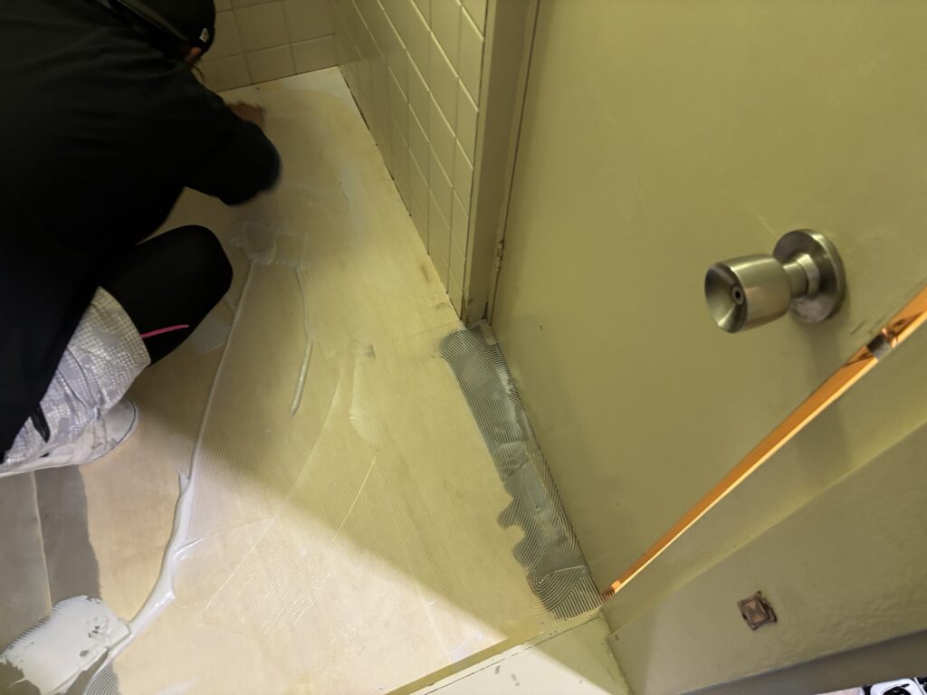 Adhesive being applied across a plywood subfloor before cushion flooring installation