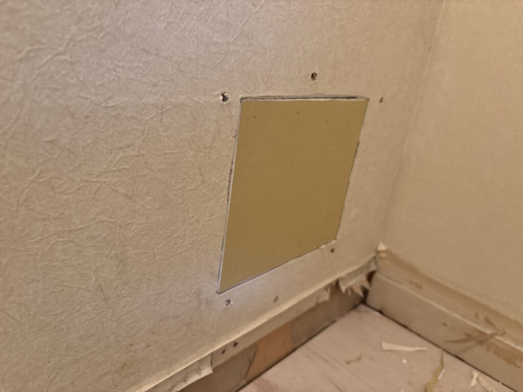 Wall beside the washing machine area with new gypsum board before partial wallpaper replacement