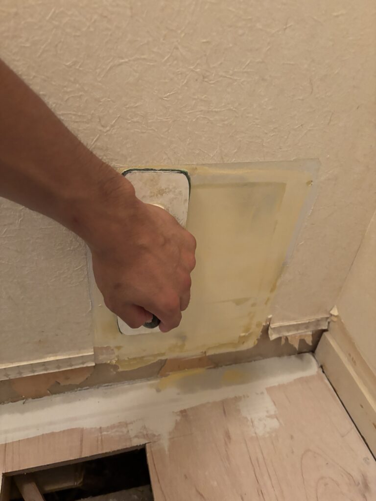 Wallpaper installer sanding finishing compound on repaired gypsum board beside the washing machine area