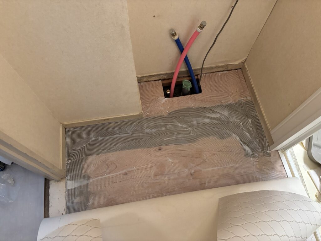 Adhesive being applied to half of a washroom floor before cushion flooring installation