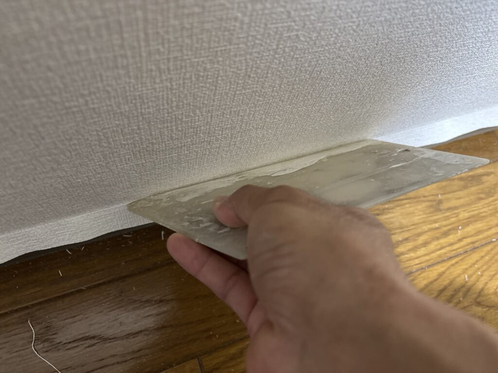 Worker using a wallpaper smoother to create a sharp corner along an existing soft baseboard