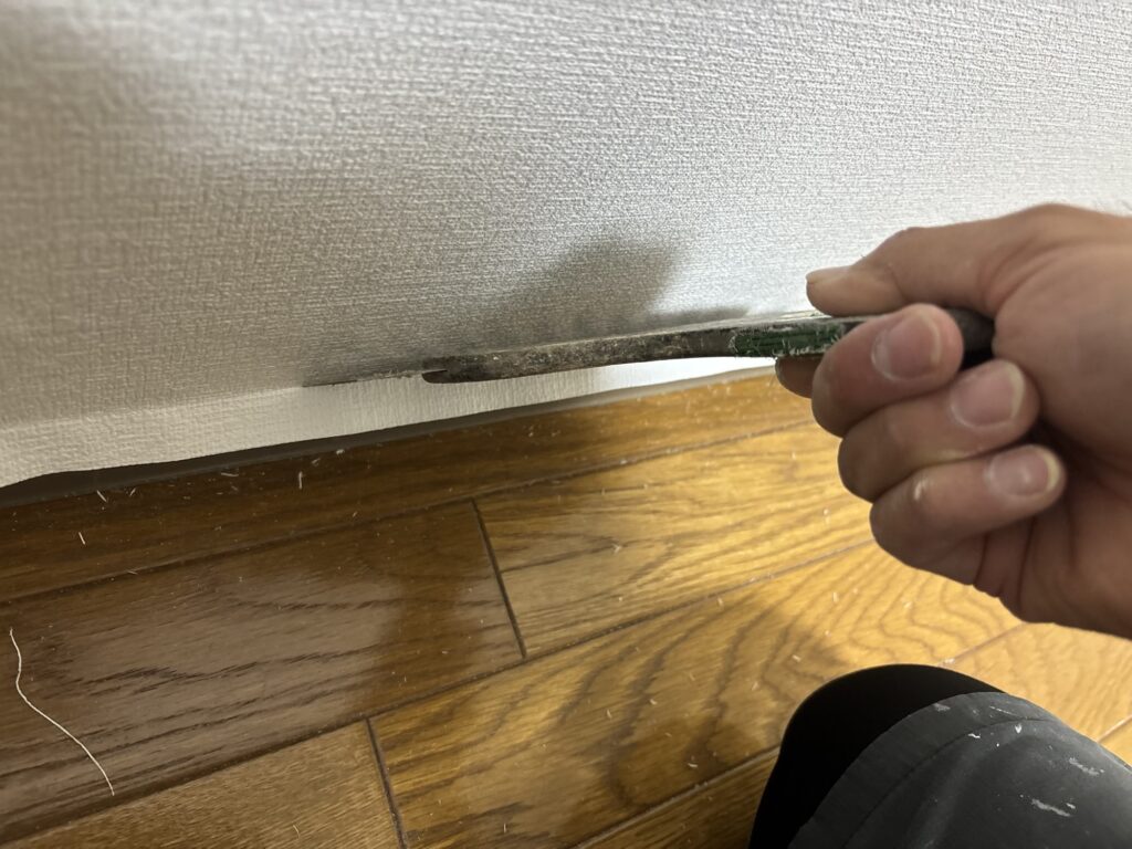 Wallpaper being trimmed along an existing soft baseboard