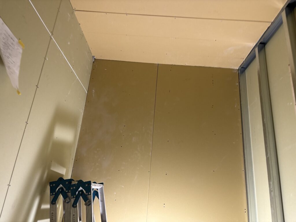 Newly installed gypsum board covering the front wall of a hotel room.
