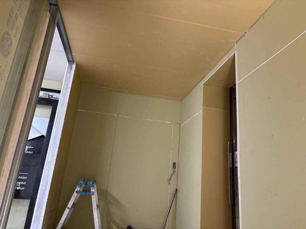 A second view of the newly installed gypsum board on the ceiling of a hotel room.