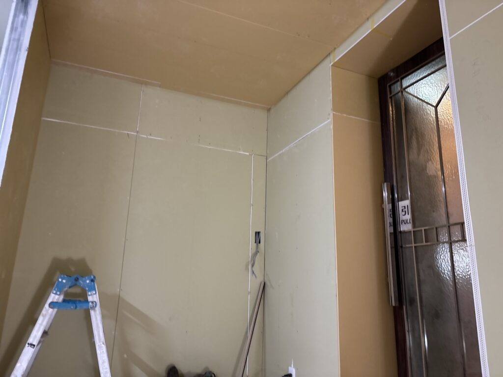 Newly installed gypsum board covering the ceiling of a hotel room during renovation.