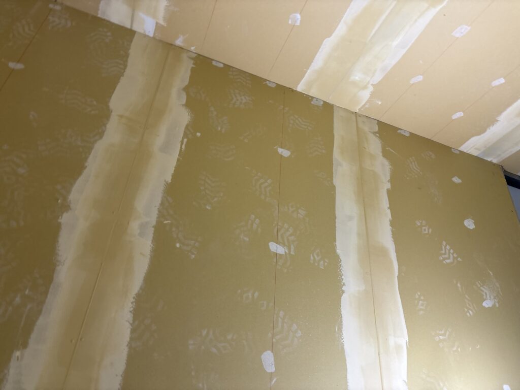 A wall surface with finishing joint compound applied and smoothed before wallpaper installation.