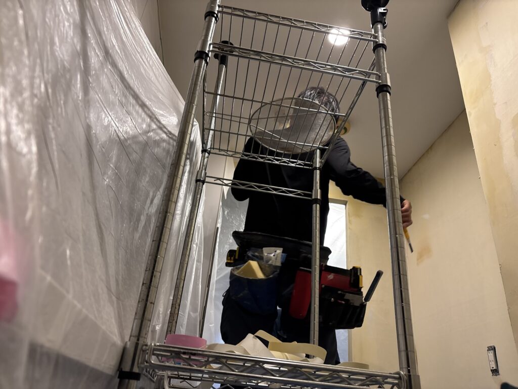 Two wallpaper installers applying wallpaper to the kitchen ceiling, working from the center toward opposite sides.