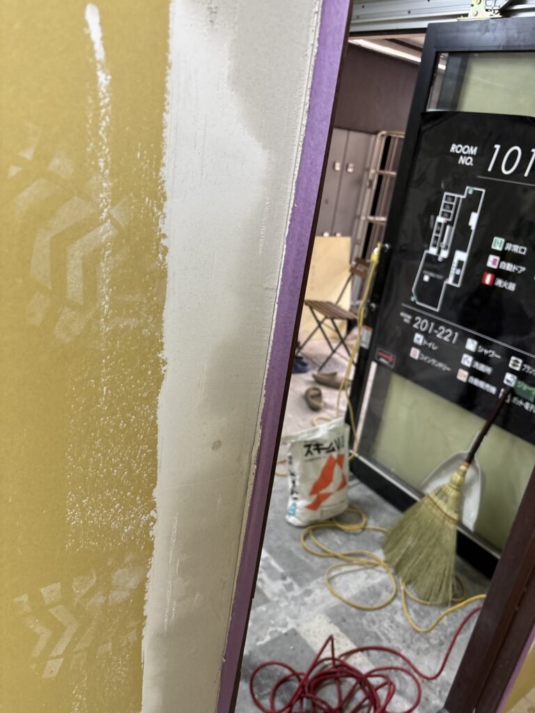 Masking tape protecting a hotel room door frame from joint compound during renovation.