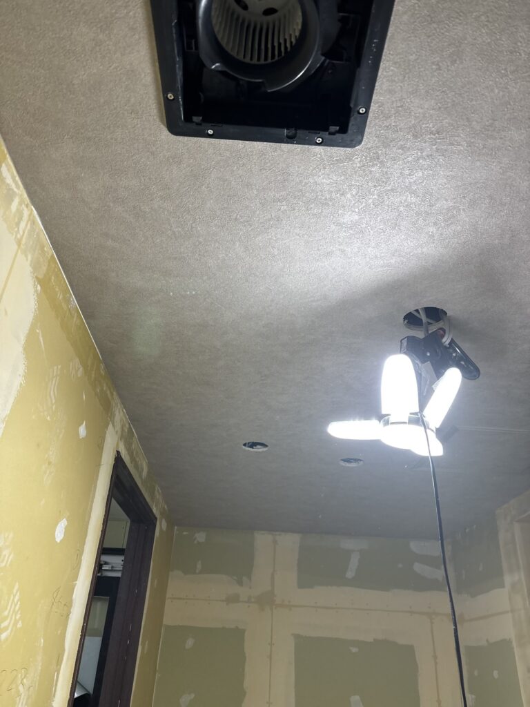 Completed gray wallpaper covering the ceiling of a hotel room.