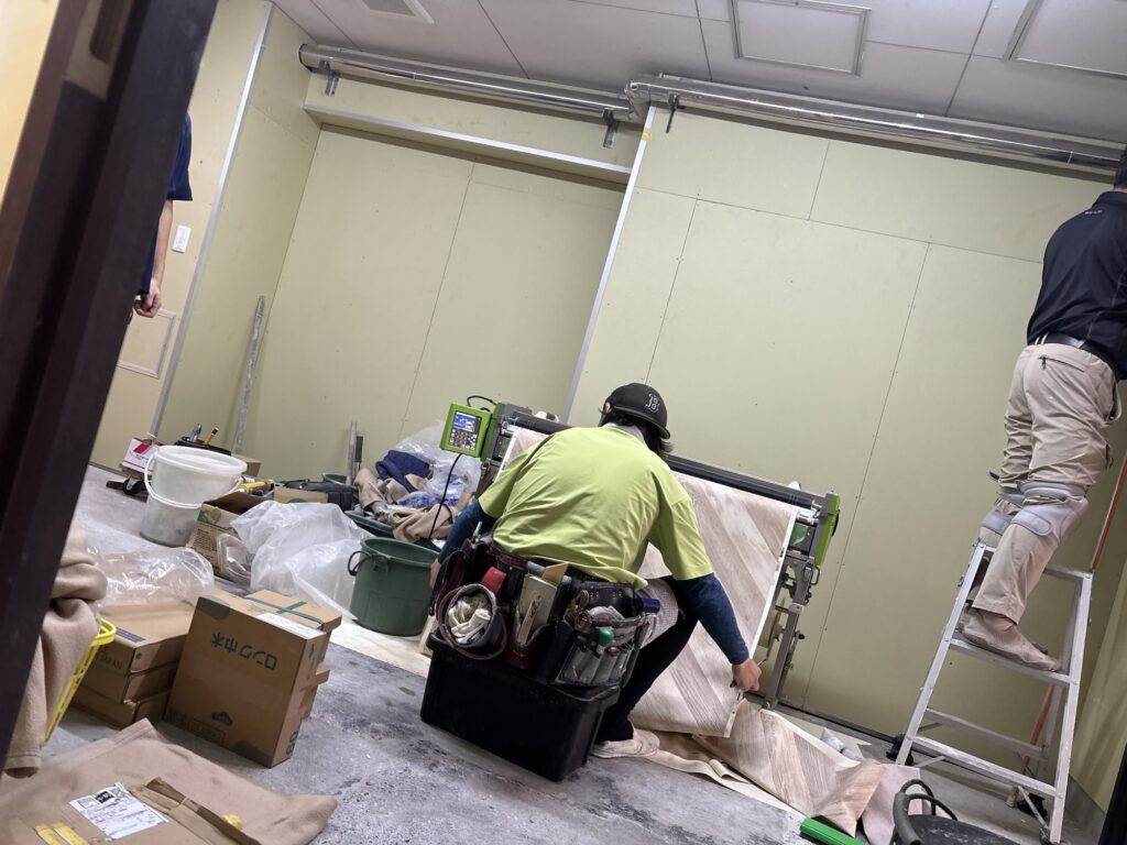 Wallpaper being fed through a wallpaper pasting machine during an interior renovation project.