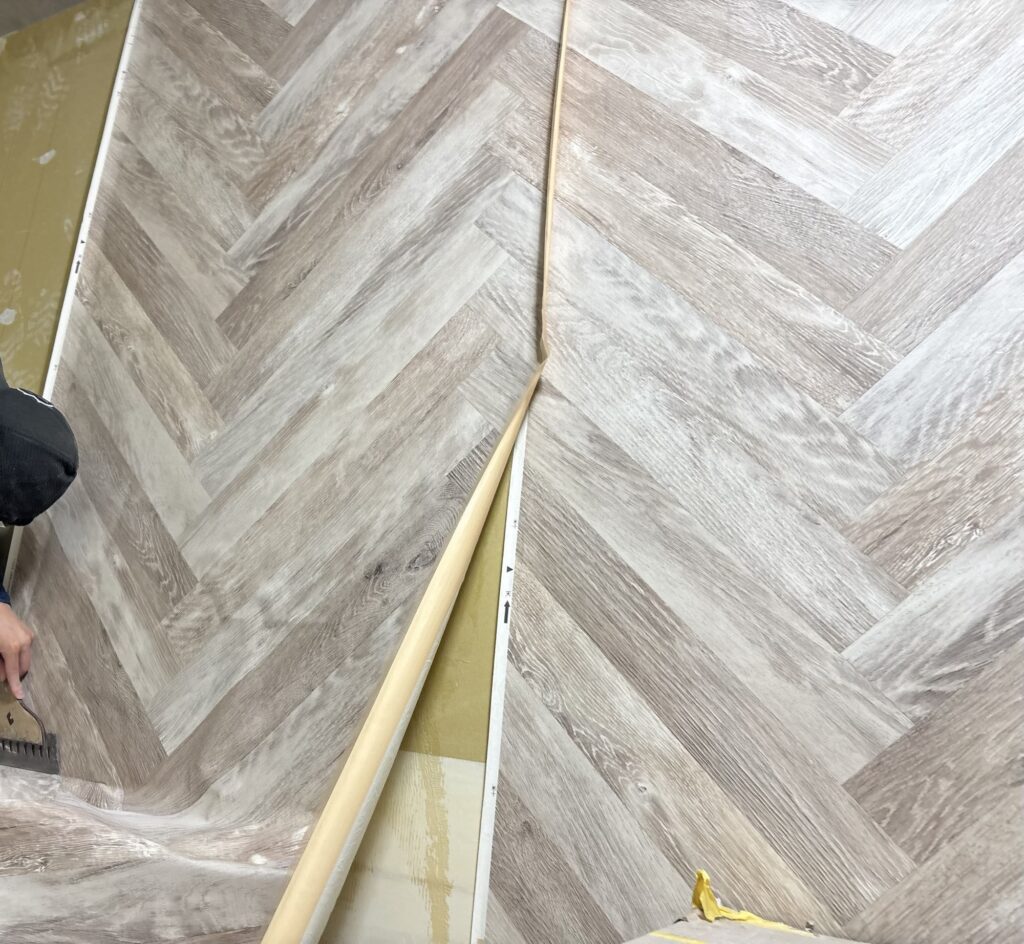 A worker installing herringbone-patterned wallpaper on an interior wall.